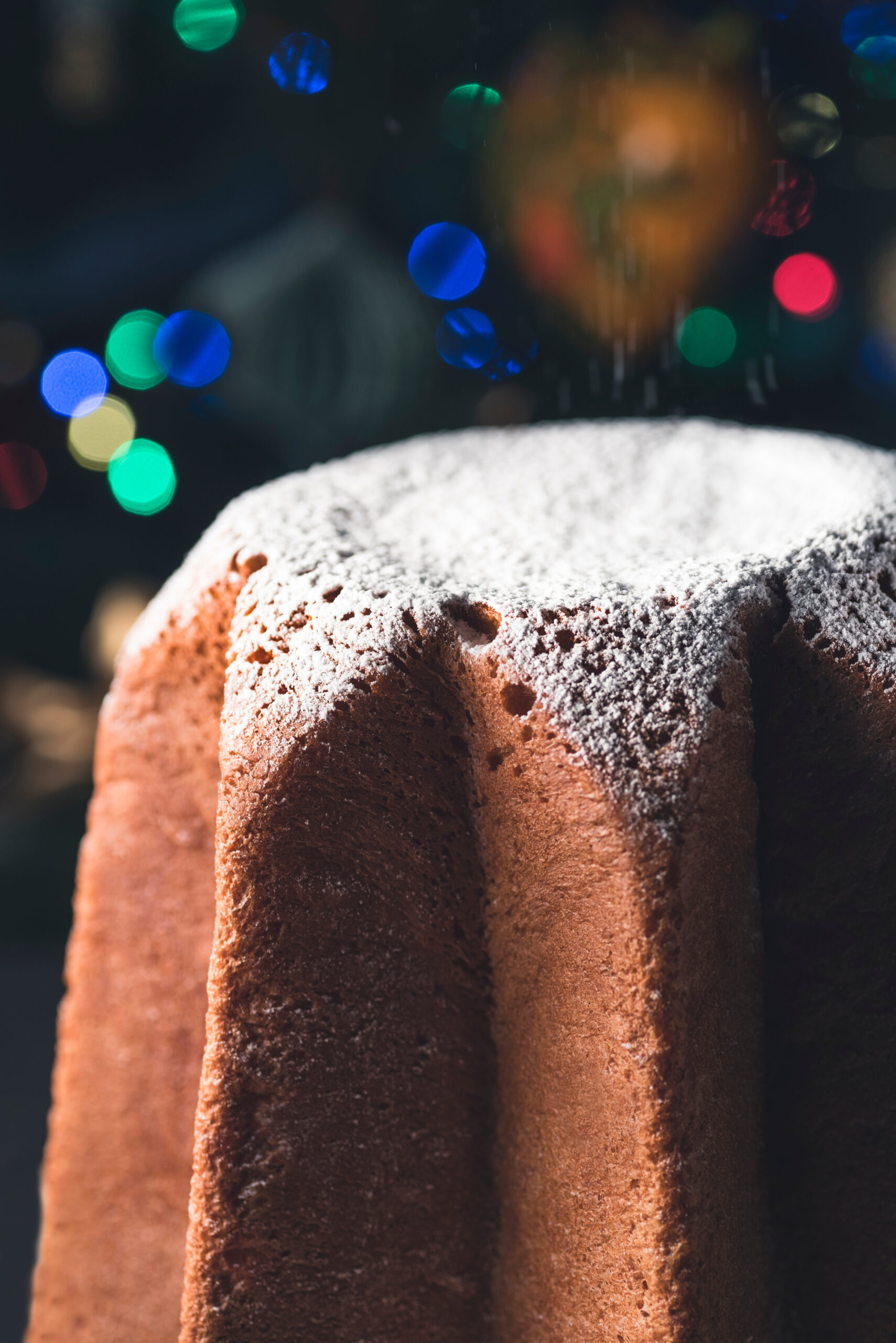 Pandoro, traditional Venetian sweet bread with powdered sugar on the festive blur background. Christmas and New Year Italian sweets. Rustic style toning, close-up